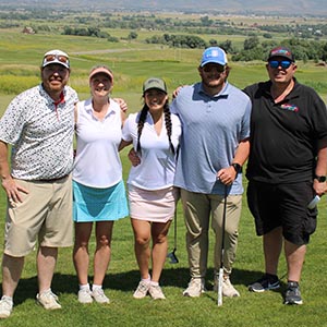 A team of five golfers smiling on a green golf course