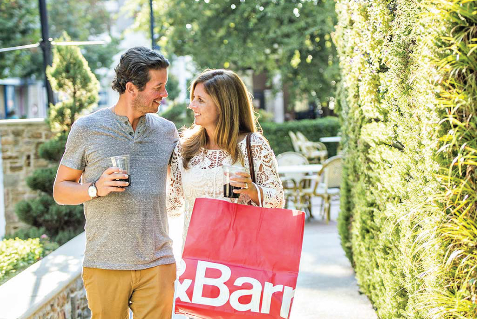 A couple with drinks and a shopping bag strolling past a green wall at Avalon