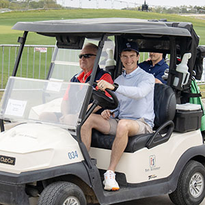 Two golfers smiling in a golf cart at the golf tournament