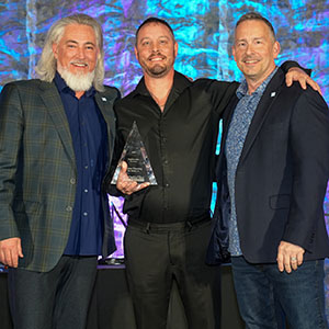 Three men on stage with a crystal award